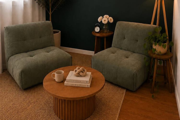 Consulting room with two olive green armchairs either side of a round timber coffee table, a dark green feature wall, an olive tree and a jute rug